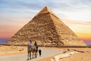 Visitors riding camels alongside Bedouins by the Pyramid of Chephren, Egypt